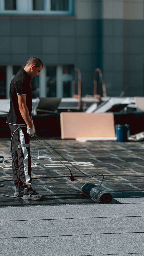 A roofer with torch equipment standing on a flat roof.