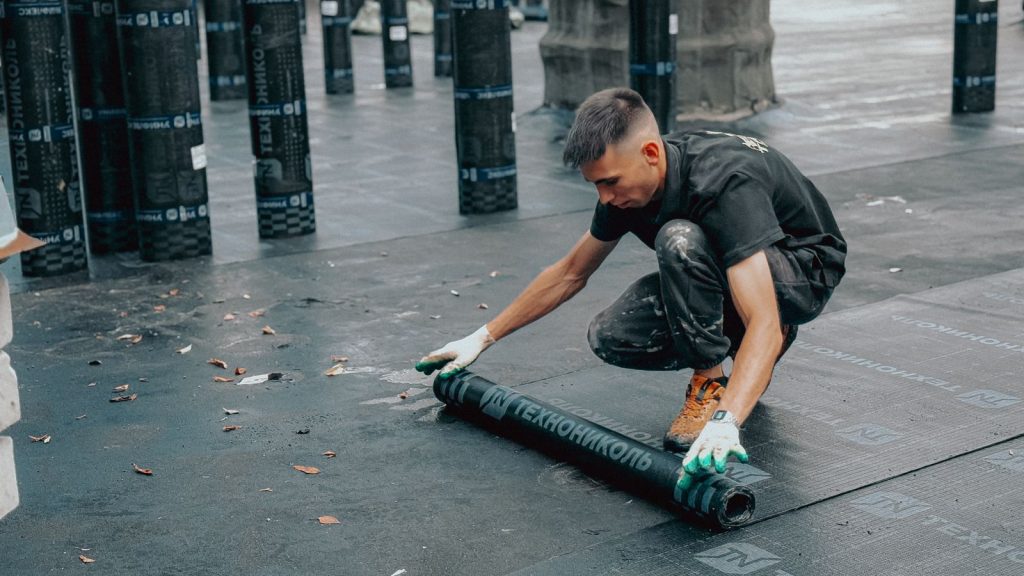A worker unrolling roofing membrane on a flat roof.