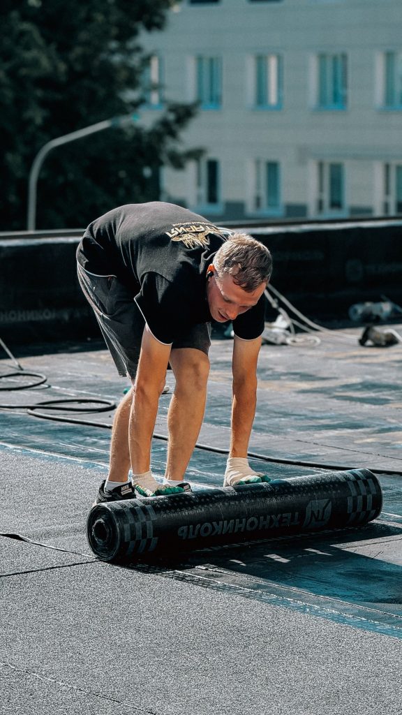 Worker unrolling a waterproof membrane across a flat roof.