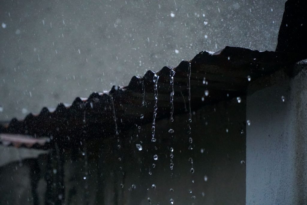 Heavy rain dripping off the edge of a roof during a storm.